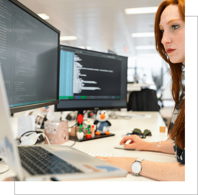 A woman sitting at her desk with two monitors.